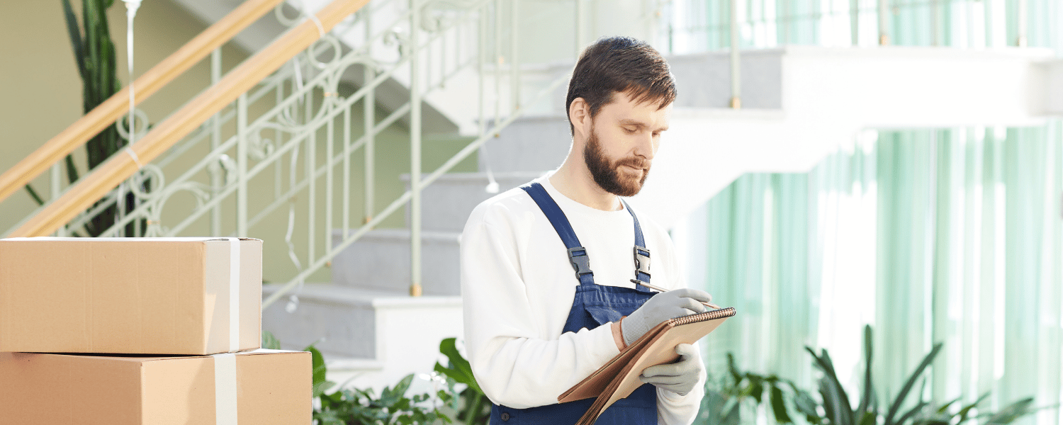 a man in overalls holding a clipboard next to boxes.