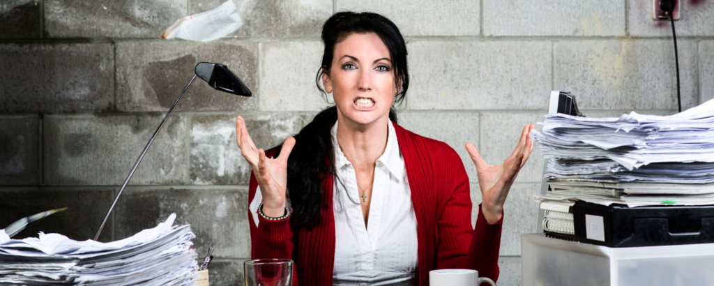 a woman making a shocked face in front of a pile of papers.